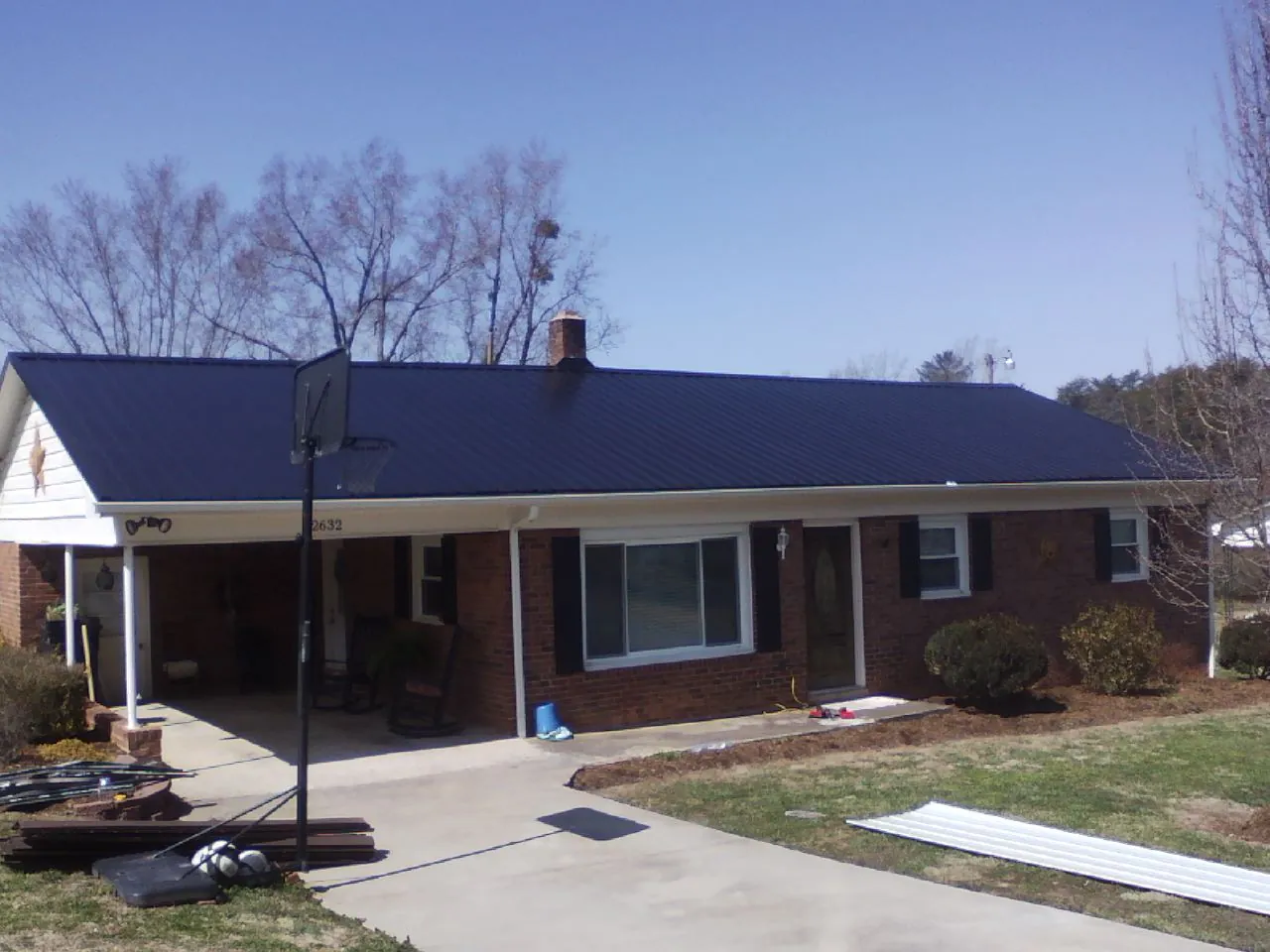 Finished dark blue metal roof on a brick ranch with a carport in Rockford