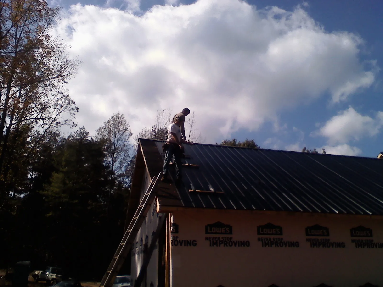 Roofer fastening dark metal panels high against a cloudy sky, from a Roof Inspection job in Rockford